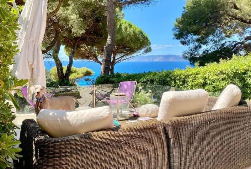 Vivienda con vistas al mar en un entorno natural, terraza con zona de descanso y muebles confortables, rodeada de árboles y vegetación, ideal para comprar o alquilar propiedades en la costa.