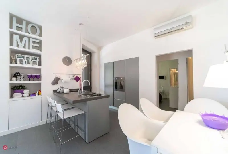 Moderno apartamento de diseño minimalista en alquiler, con cocina abierta, muebles blancos, electrodomésticos integrados y decoración elegante. Ideal para vivir en un entorno confortable y sofisticado.