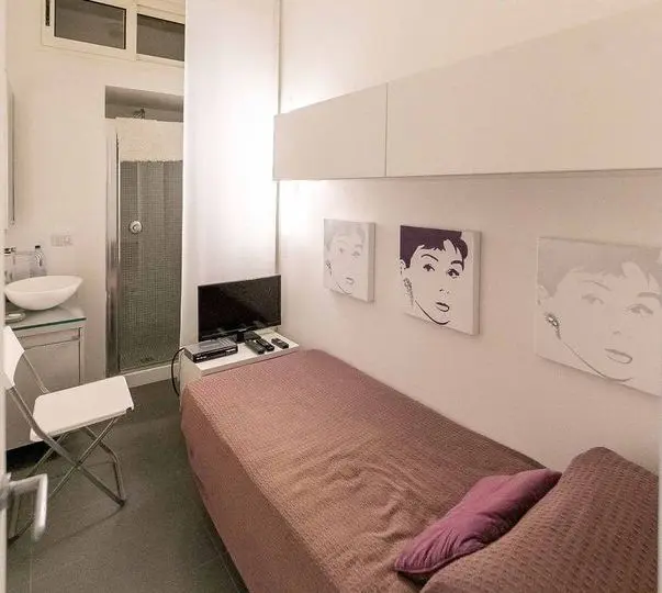 Habitación moderna y luminosa en apartamento en alquiler, con cama individual, decoración minimalista, televisión, ventilador de techo, y espacio para actividades en ambiente acogedor en zona residencial.