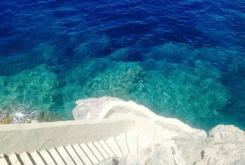 Escalera en la playa con vista al mar cristalino, ideal para propiedades en zonas costeras y de lujo, perfecta para invertir en bienes raíces en destinos soleados y de alta demanda.