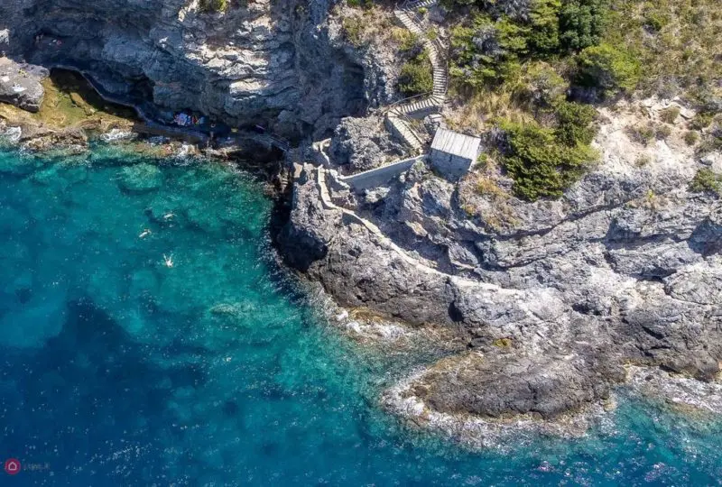 Vivienda junto al mar en una escarpada costa rocosa con acceso mediante escaleras de madera, rodeada de vegetación y con vistas panorámicas al océano, ideal para inversión inmobiliaria y propiedades de lujo.