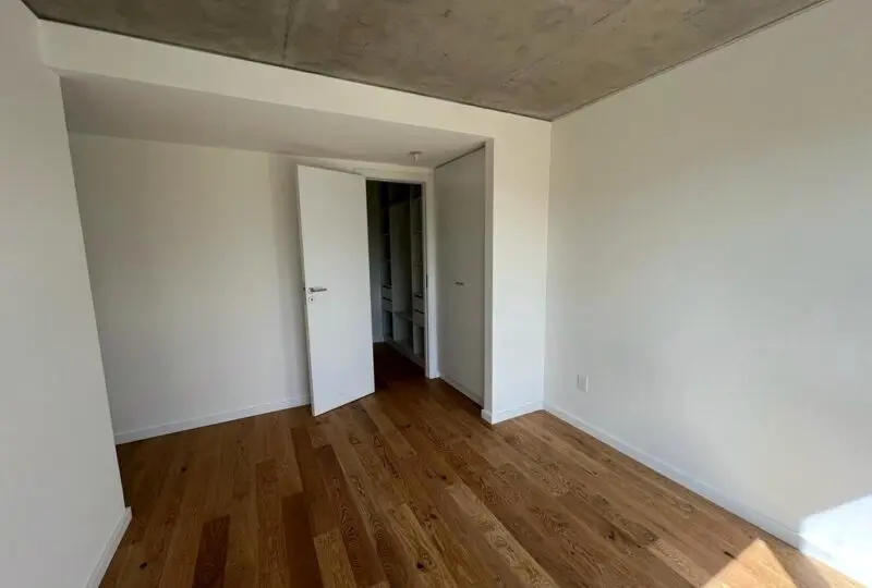 Habitación vacía en propiedad en alquiler o venta, con paredes blancas, suelo de madera y ventana que permite la entrada de luz natural, ideal para residencias modernas y espaciosas.