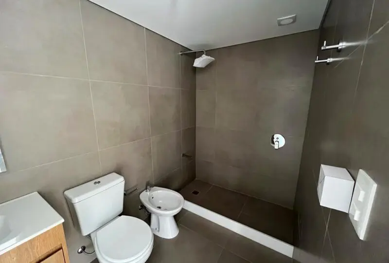 Limpia y moderna ducha en baño de apartamento en venta, con azulejos gris claro y accesorios elegantes. Perfecta para hogares que buscan funcionalidad y estilo en la propiedad.