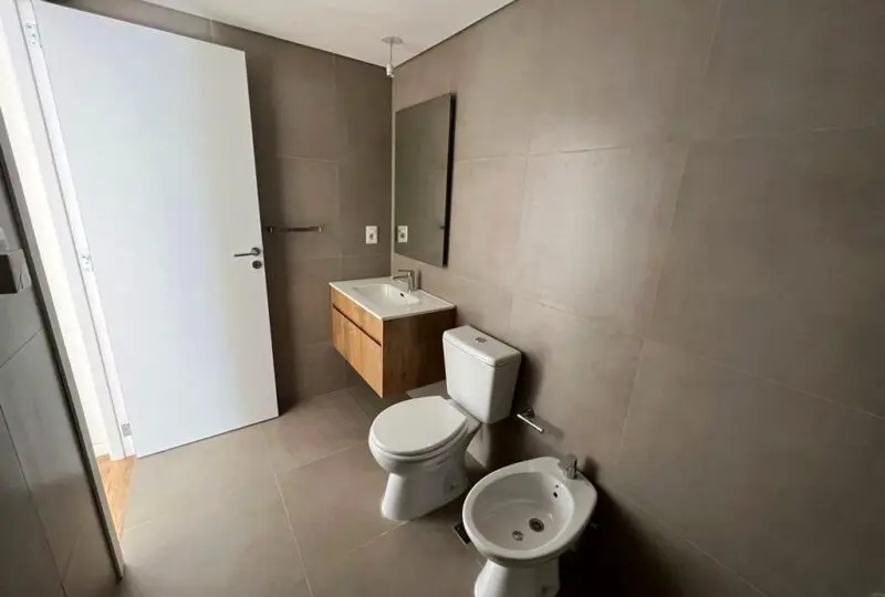 Baño moderno en vivienda en alquiler o venta con azulejos en tonos neutros, lavabo de madera, espejo grande, inodoro y bidé, ideal para ofrecerte comodidad y funcionalidad en tu hogar o inversión inmobiliaria.