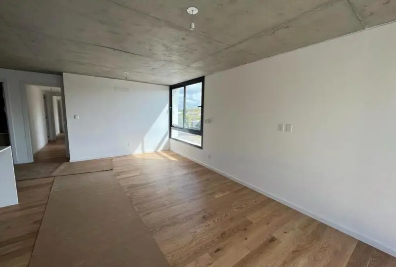 Amplio salón luminoso con ventanas grandes y pisos de madera en una propiedad en desarrollo, ideal para inversión y compra de viviendas, de Horus Agencia Inmobiliaria en España.