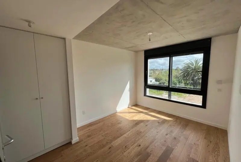 Amplio dormitorio con ventana grande en Horus Real Estate Agency Moderno dormitorio con ventana grande y vistas a la naturaleza, suelo de madera y paredes blancas, ideal para vivir con confort y estilo.