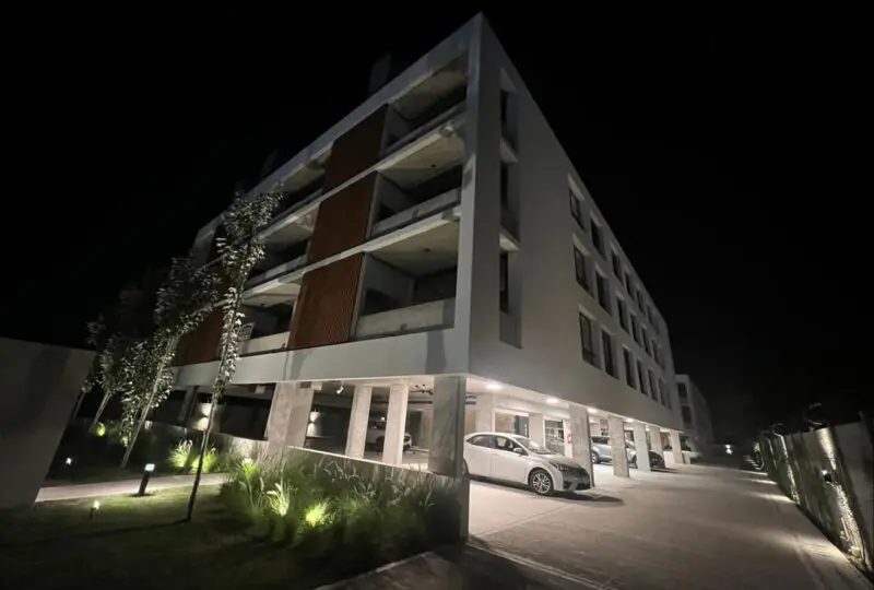 Edificio moderno de apartamentos en venta o alquiler en Horus Real Estate Agency, con estacionamiento subterráneo, iluminación exterior y jardines bien cuidados.