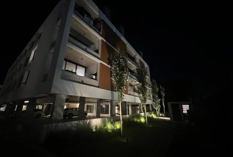 Moderno edificio residencial con iluminación nocturna, fachada contemporánea y departamentos con amplios balcones, ideal para inversión inmobiliaria en Horus Real Estate Agency.