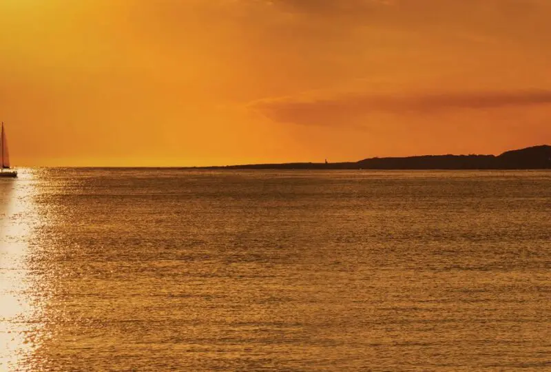 At alt text only: Atardecer en la costa con barco y cielo naranja, vistas de bienes raíces en Horus Real Estate Agency en la Costa de España.