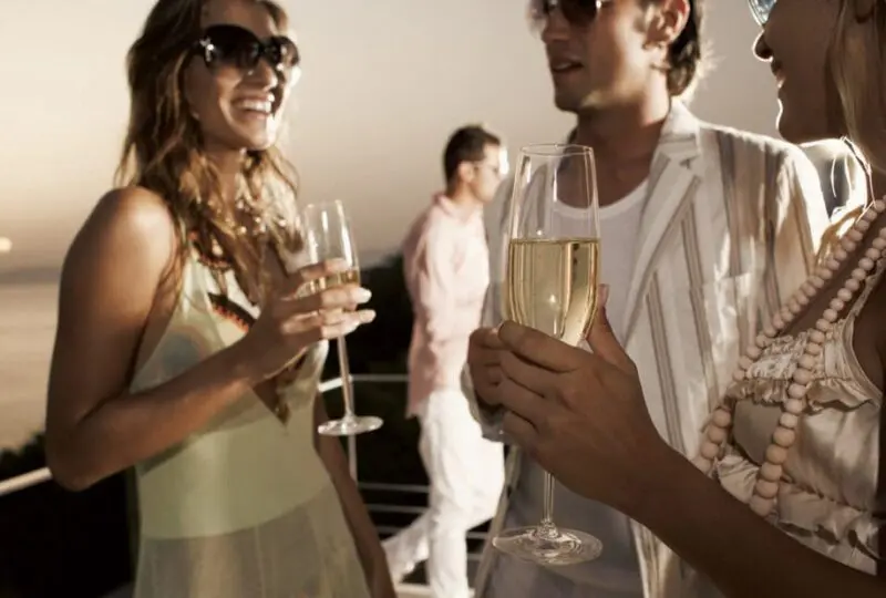 Relaciones sociales en evento exclusivo con vistas al mar, celebración y networking en un ambiente sofisticado y elegante. Personas brindando con champán en terraza al atardecer, estilo de vida de alto nivel.