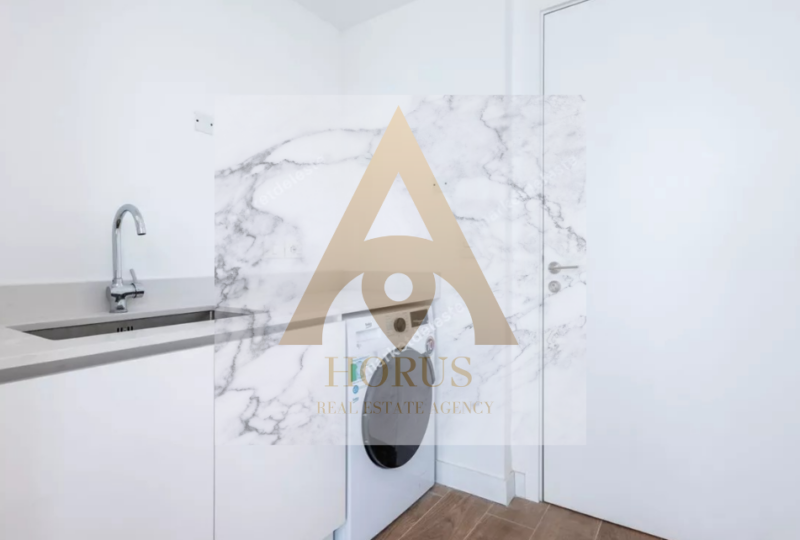 Lavadora en zona de lavandería con encimera de mármol y fregadero, espacio funcional y moderno, en un inmueble gestionado por Horus Agencia Inmobiliaria.