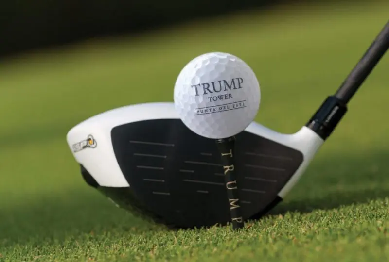 Golf club y pelota con logo del Trump Tower Punta del Este, en un campo de golf bien cuidado.