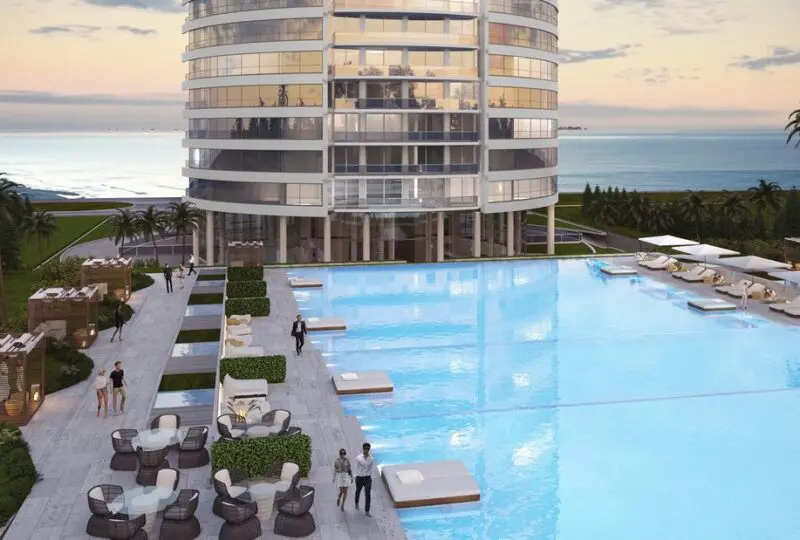Luxurious modern residential building with swimming pool and outdoor seating area, overlooking the ocean, ideal for premium real estate investment and beachfront living.