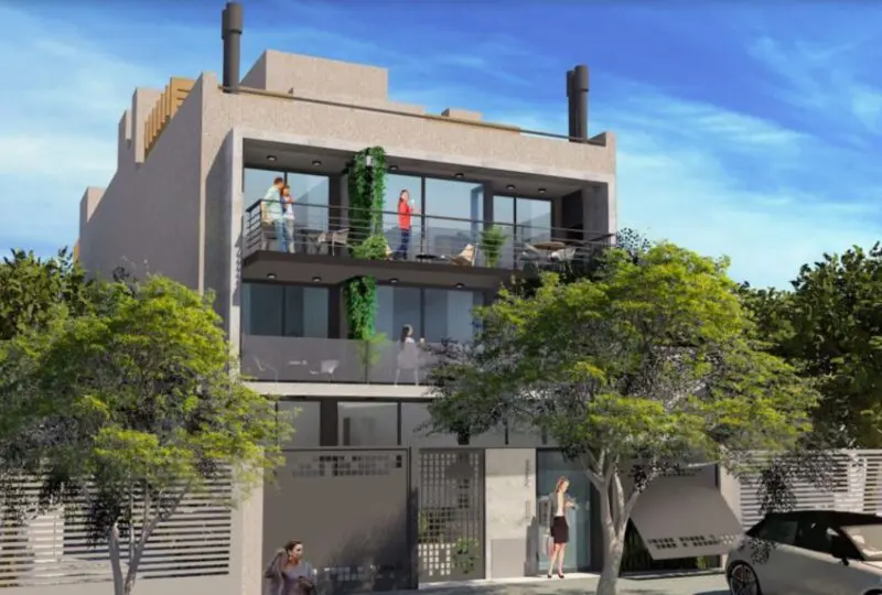 Amplia fachada moderna de edificio residencial con balcones y terrazas, rodeado de árboles y zona urbana, ideal para inversión inmobiliaria en la ciudad.