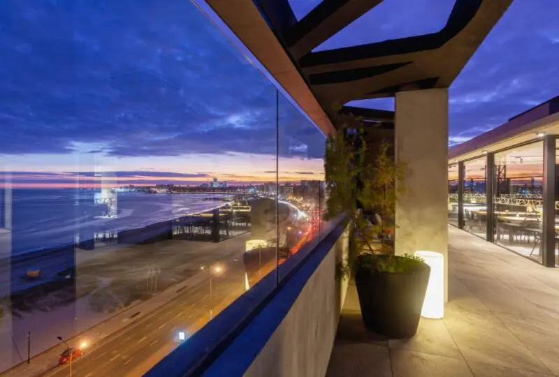 Vistas panorámicas al atardecer desde un balcón moderno en Horus Real Estate Agency con vista al mar y la ciudad, ideal para propiedades exclusivas en la costa.