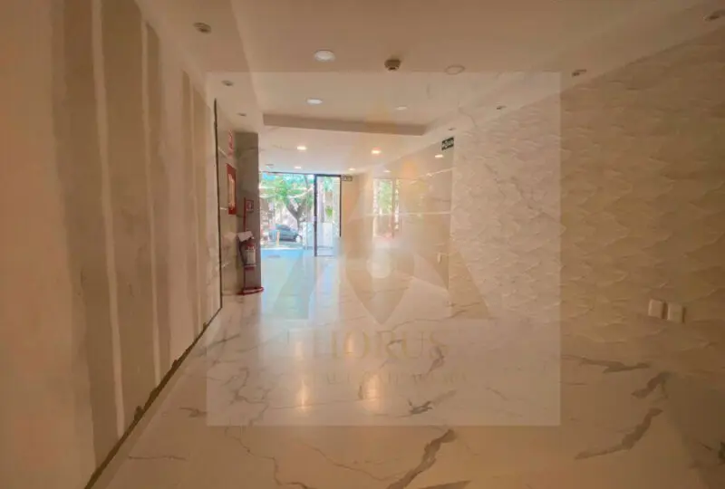 Puerta de entrada a la oficina de la agencia inmobiliaria Horus con interior moderno y luminoso, mármol en suelos y paredes decorativas, ubicada en una zona con vistas a la calle y luz natural.