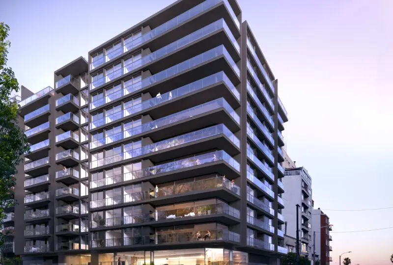 Amplio edificio residencial moderno con balcones de cristal en primer plano, ubicado cerca del mar en un entorno urbano, ideal para inversión y vida en la playa.
