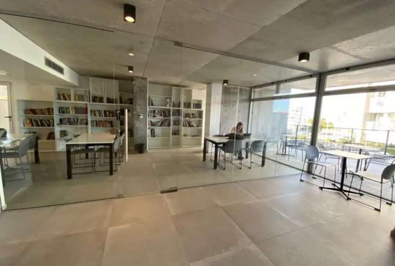 Espacio de oficina moderna con paredes de cristal, estanterías llenas de libros y mobiliario funcional, ideal para negocios y coworking en un entorno profesional.
