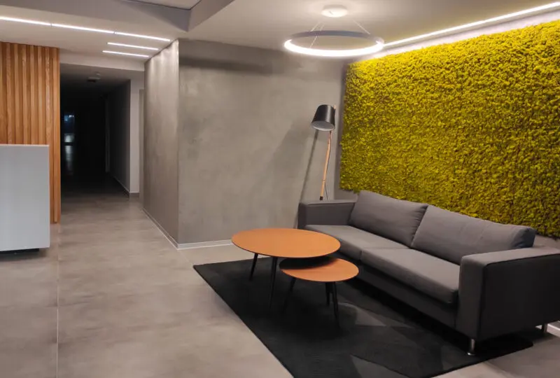 Sofá gris moderno en vestíbulo de hotel o edificio de oficinas con pared de musgo decorativa y lámpara de pie, ambiente elegante y acogedor.