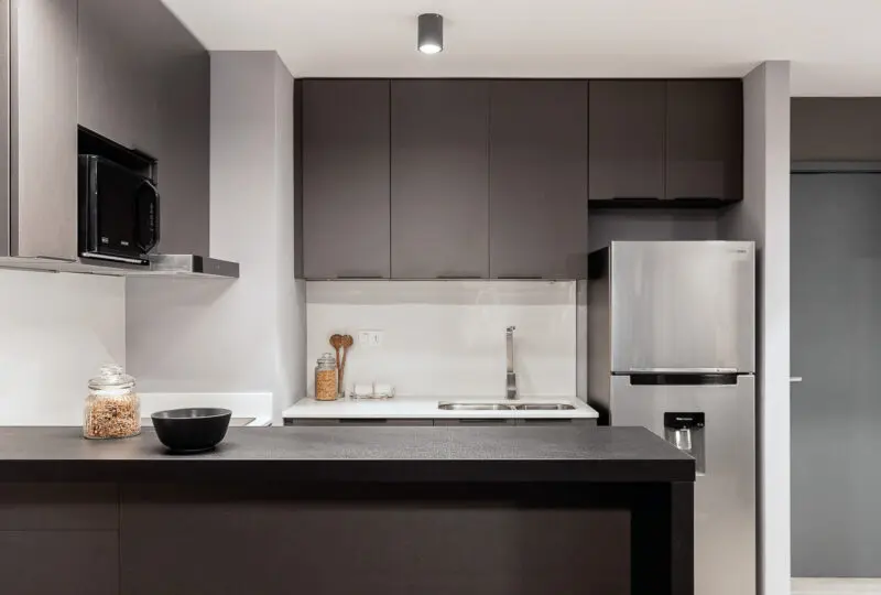 Moderno diseño de cocina en apartamento de alquiler, equipado con electrodomésticos en acero inoxidable, gabinetes oscuros y encimera de granito para estilo urbano y funcionalidad.