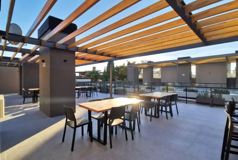 Vistas de una terraza moderna con mobiliario para eventos, techo de madera y estructura metálica, ideal para reuniones y celebraciones en propiedades exclusivas de Horus Inmobiliaria.