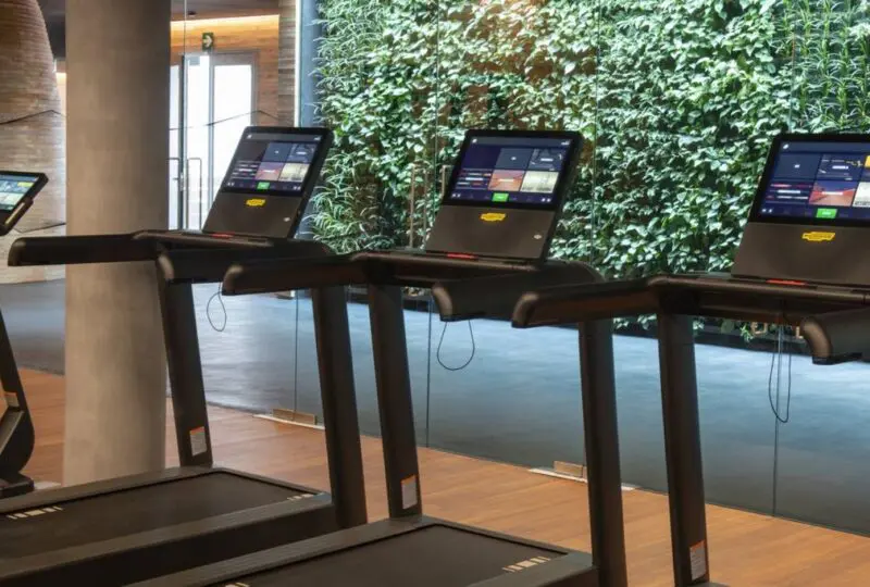Cintas de correr en un gimnasio moderno con paredes verdes y ambiente luminoso en Horus Real Estate Agency.