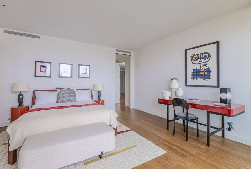 Amplio dormitorio en apartamento elegante, con decoración moderna, mesitas de noche con lámparas, escritorio con silla y obras de arte, ideal para inversores en bienes raíces y clientes de agencia inmobiliaria Horus.