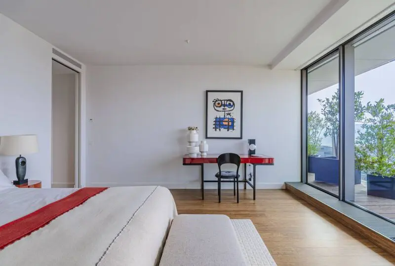 Amplio dormitorio moderno con balcón y vista a la terraza, equipado con mobiliario elegante, suelo de madera y decoración minimalista, ideal para vivir en un apartamento de lujo.