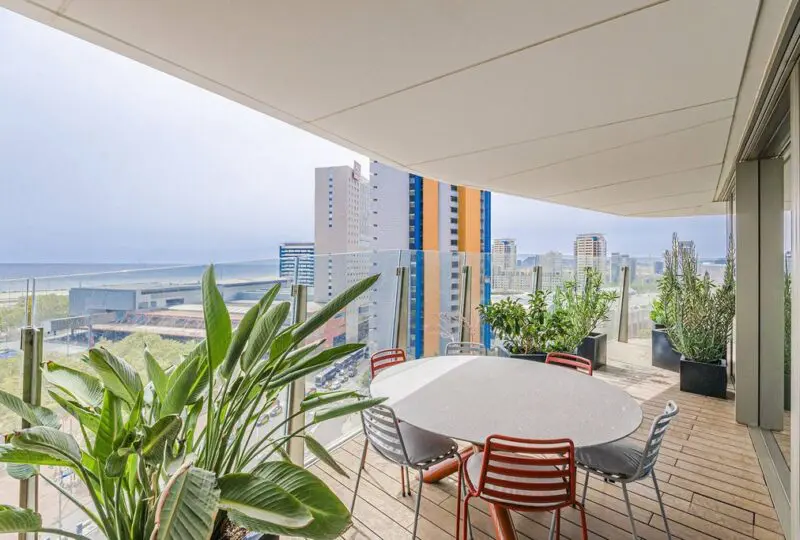 Vistas panorámicas desde terraza en vivienda de lujo en la ciudad, con muebles de exterior y plantas decorativas, perfecta para disfrutar del sol y la comunidad en un entorno exclusivo.