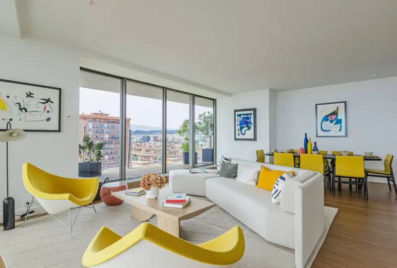 Amplia sala de estilo moderno con grandes ventanas, muebles elegantes y decoración colorida, perfecta para residencias en Barcelona y costa de España.