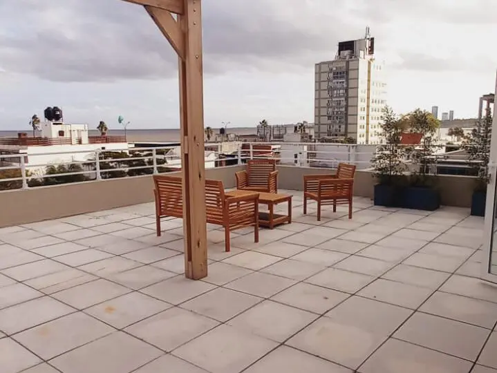 Amplia terraza en edificio residencial con estructura de madera para sombra, muebles de exterior y vistas despejadas a la ciudad. Ideal para relajarse y socializar en un espacio privado y moderno.