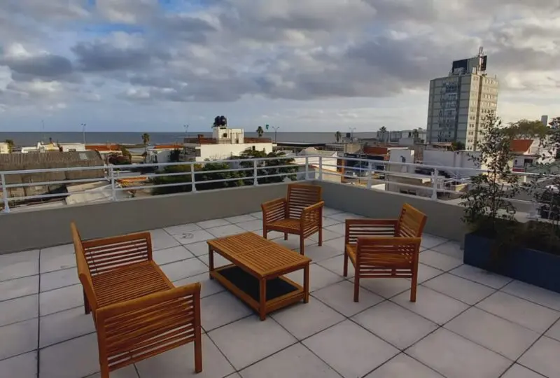 Terraza con vistas al mar en un edificio moderno en la ciudad, mobiliario de madera para relajarse, espacio exterior para reuniones, imagen de agencia inmobiliaria Horus Real Estate Agency, propiedades en venta y alquiler en zonas urbanas.
