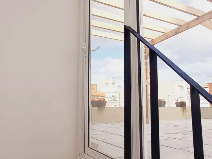Puerta balconera de espacio interior hacia terraza con vista a cielo y edificios, ideal para propiedades modernas y luminosas.