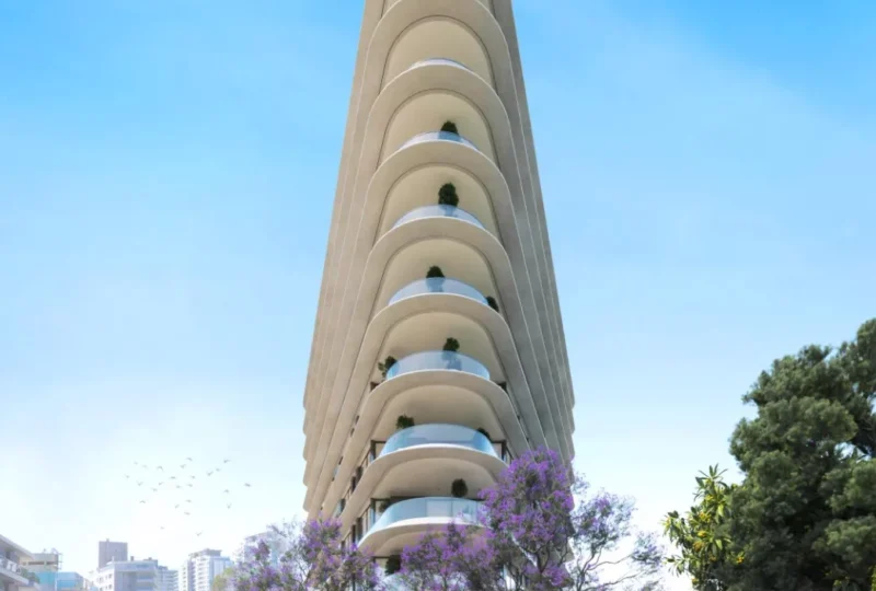 Edificio de apartamentos moderno con balcones curvos y jardines en las terrazas, en una zona urbana con árboles y áreas verdes, ideal para inversión inmobiliaria en la ciudad.
