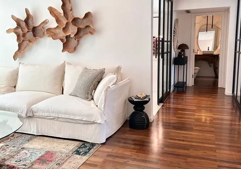 Moderno salón de apartamento en venta con decoración minimalista, paredes blancas, suelo de madera natural, obras de arte en la pared y ambiente acogedor en zona residencial de lujo.