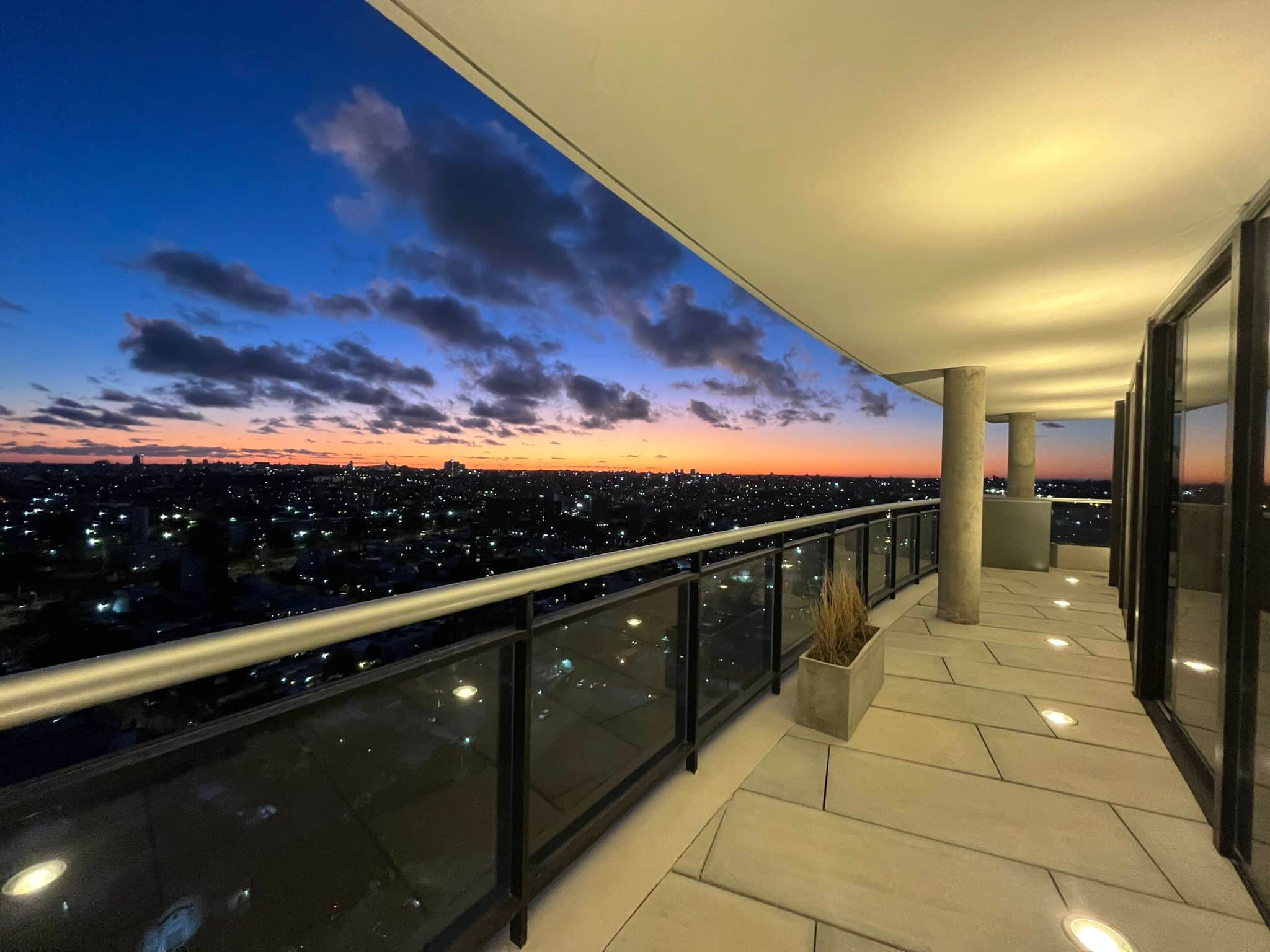 Vistas panorámicas desde un balcón de lujo en un rascacielos moderno en la ciudad al atardecer, ideal para propiedades de alto standing en venta o alquiler en el sector inmobiliario de lujo.