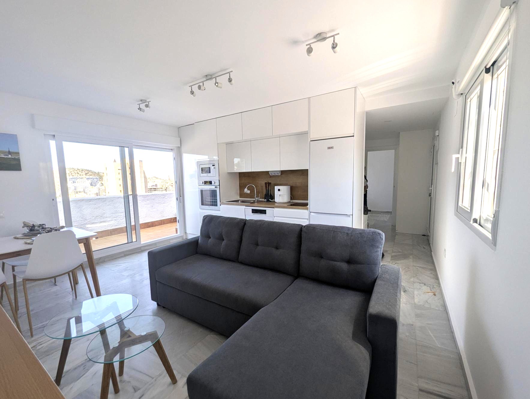 Moderno salón con cocina equipada y zona de comedor en apartamento en alquiler en la Costa Blanca. Espacioso y luminoso, ideal para vivir cerca de la playa con estilo y comodidad.